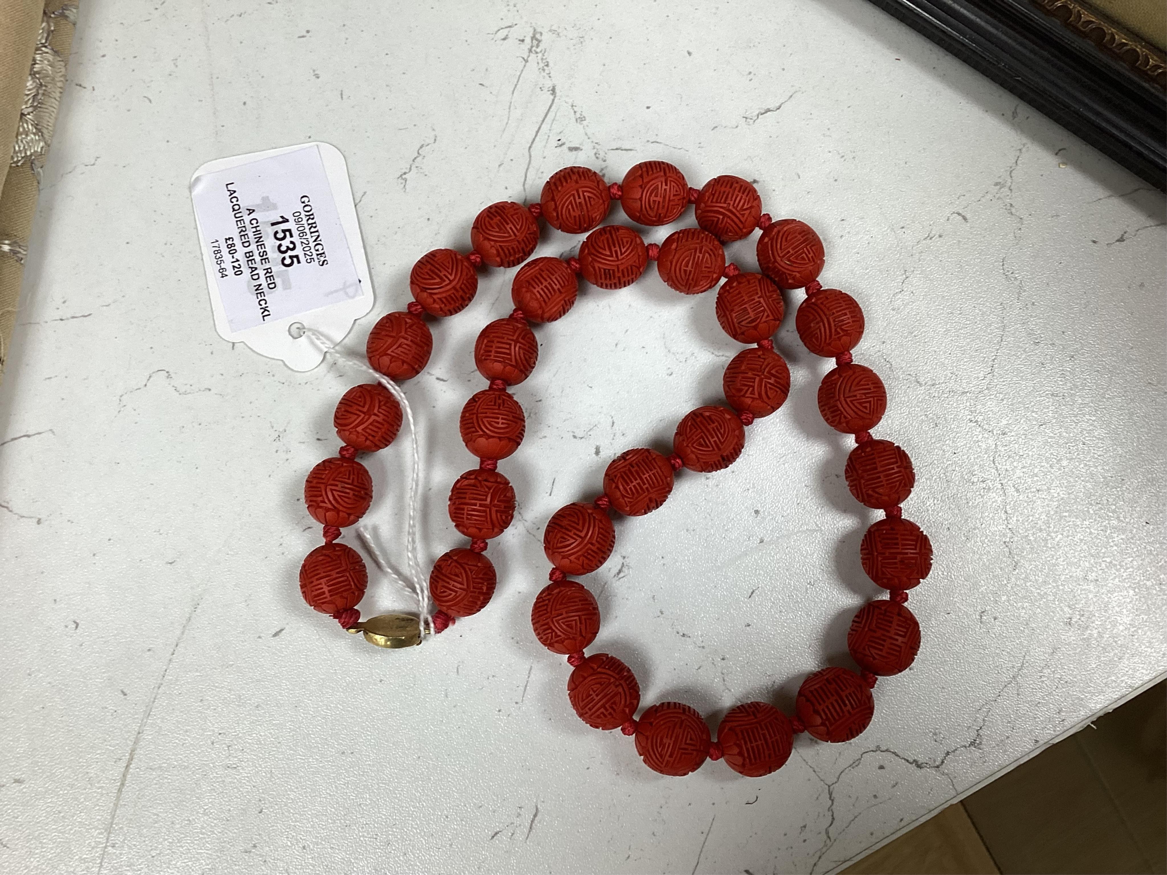 A Chinese red lacquered bead necklace and a bowenite jade figure of a cat